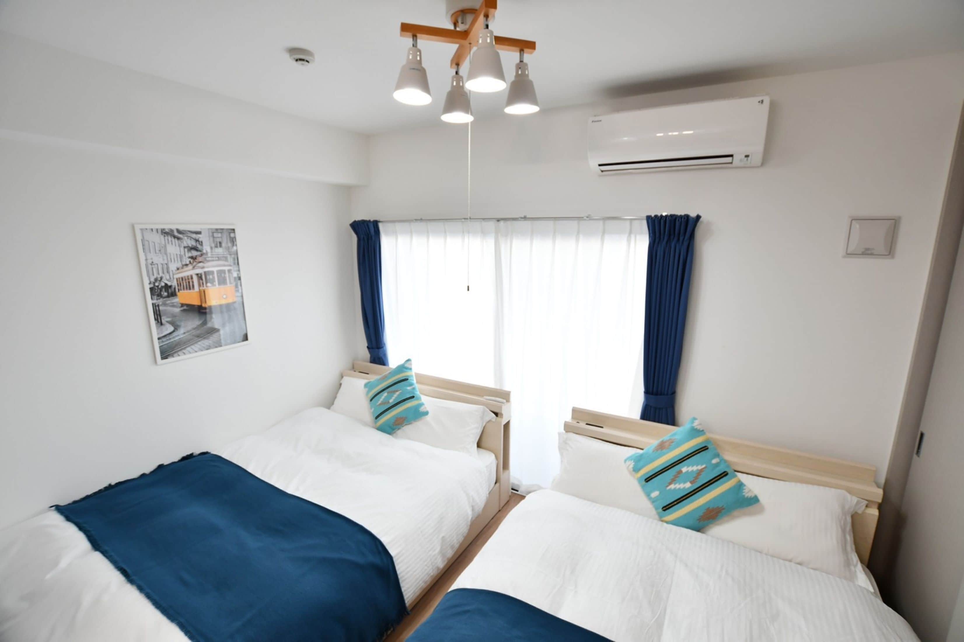 Habitación de hotel con dos camas, una ventana con cortinas, un equipo de aire acondicionado y una lámpara en el techo.