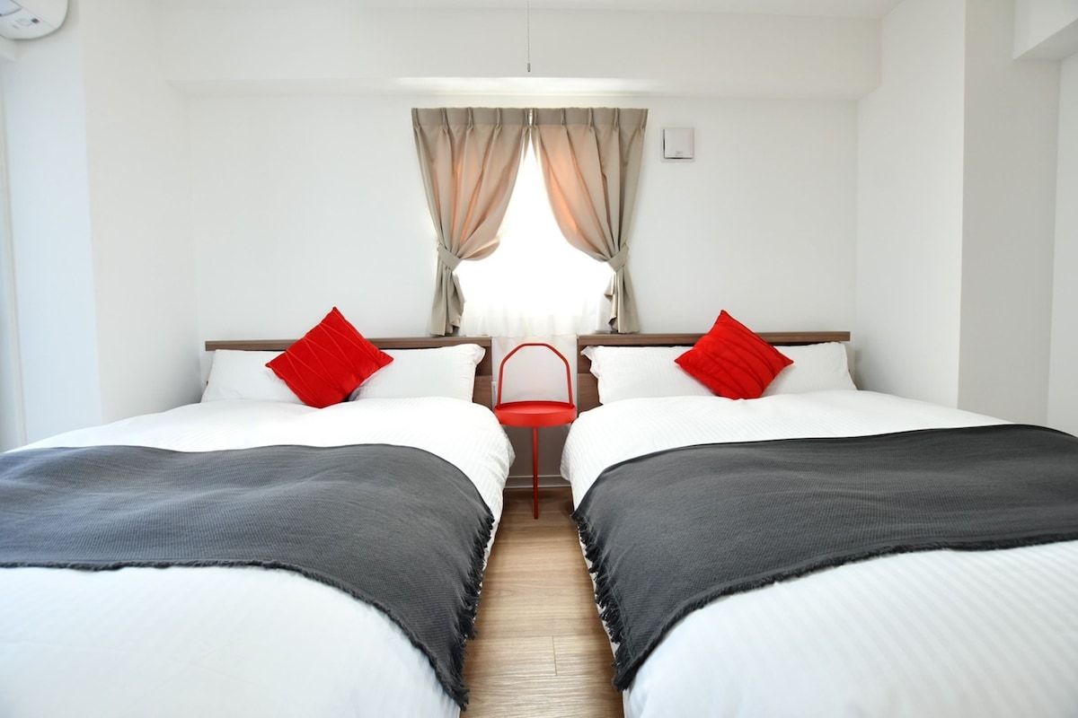 Une chambre d’hôtel avec deux lits, une petite table et une fenêtre avec des rideaux.
