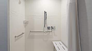 A modern bathroom with white tiles, a shower with a handheld showerhead, a towel rack, and a small table.