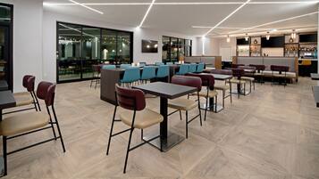 A modern dining area with tables and chairs, a bar area with shelves of bottles, and a large glass wall with a view.