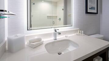 A modern bathroom with a white sink, a glass shower enclosure, and a framed picture on the wall.