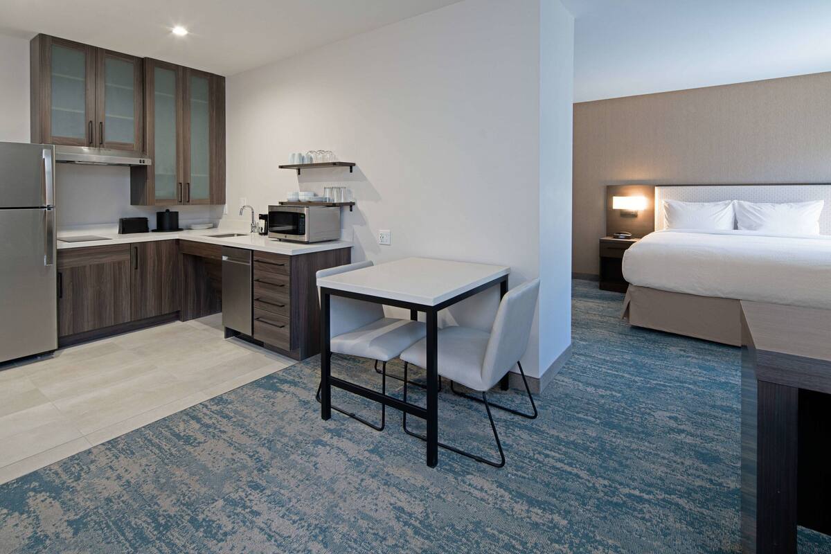 A compact hotel room with a kitchenette, a single bed, and a small table with chairs.
