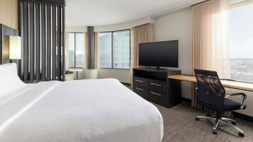 A hotel room with a large bed, a desk with a computer, a TV, and a view of the city.