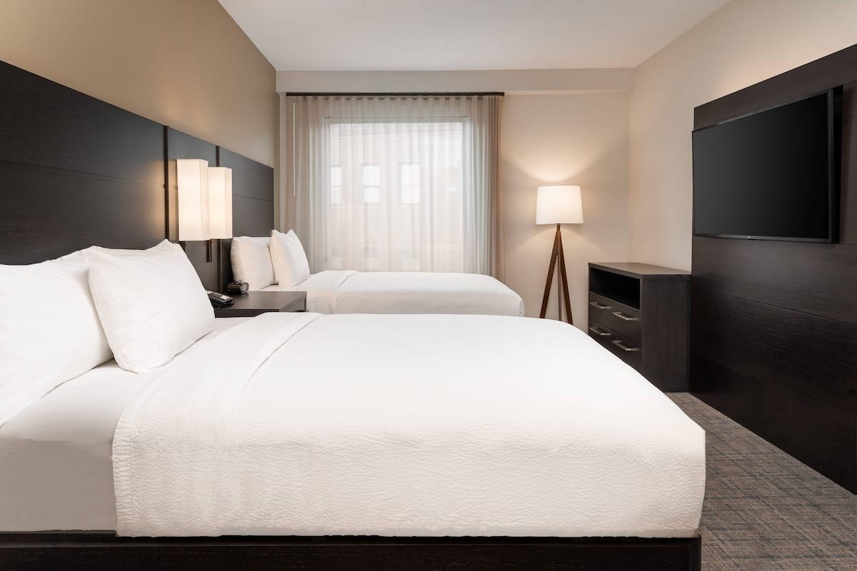 Een hotelkamer met een groot bed, twee nachtkastjes, een televisie en een raam met gordijnen.
