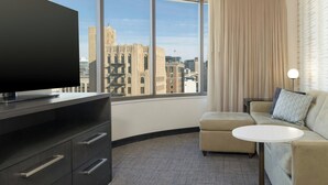 A hotel room with a large window, a flat-screen TV, a sofa, a small round table, and a minibar. - Residence Inn by Marriott Grand Rapids Downtown (Grand Rapids)