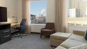 Habitación de hotel con un ventanal grande, un escritorio con silla, un sofá y un televisor.
