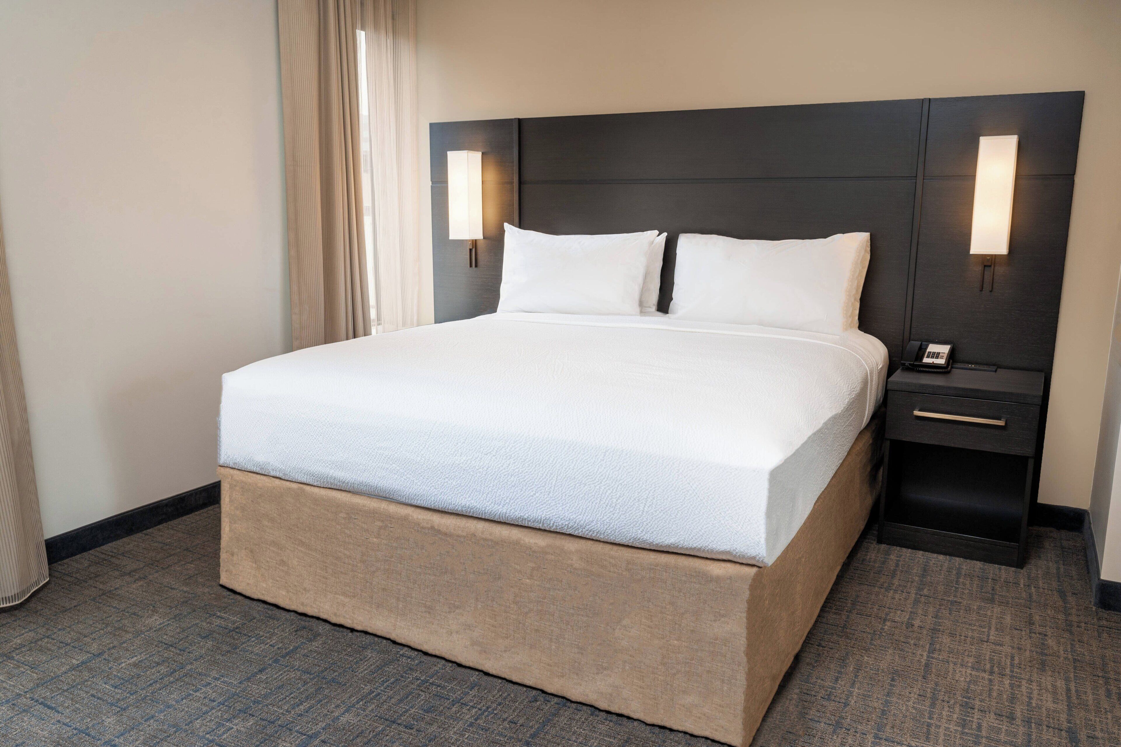 Een hotelkamer met een groot bed, een nachtkastje met een telefoon en een wandlamp.