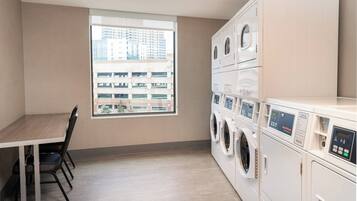 A laundry room with a table and chairs, a large window, and stacked washing machines.