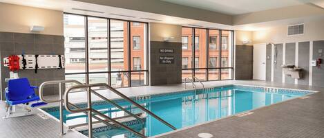 Una piscina interior amb indicació clara, una cadira de socorrista i una vista de l'edifici exterior.