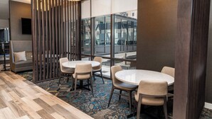 A modern meeting room with round tables and chairs, a patterned carpet, and large windows offering a city view. - Residence Inn by Marriott Grand Rapids Downtown (Grand Rapids)