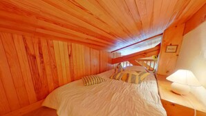 Um quarto aconchegante com teto de madeira, uma cama com roupa de cama branca e uma mesa de cabeceira com abajur.