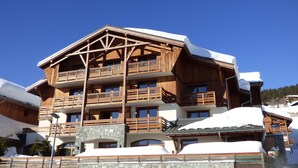 Un bâtiment en bois à plusieurs étages, doté de balcons, d’une fondation en pierre et entouré d’un paysage enneigé.