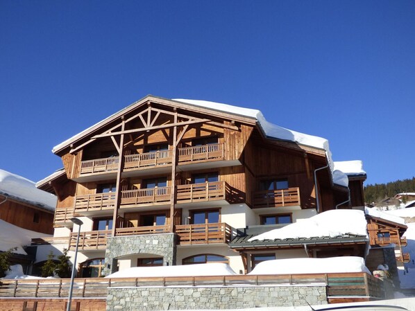 A multi-story wooden building with balconies, stone foundation, and snow-covered surroundings.