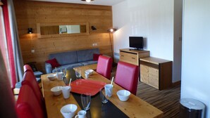 Une pièce moderne avec un mur en bois, un canapé, une table à manger avec des chaises, un téléviseur posé sur un meuble en bois et un miroir accroché au mur.