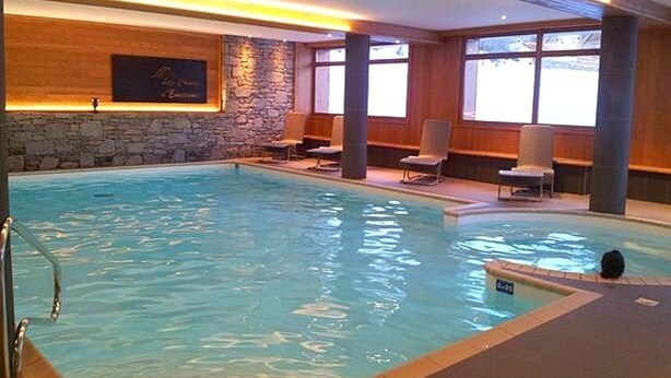 Une piscine intérieure avec un mur en pierre, un lambris en bois et plusieurs chaises longues.