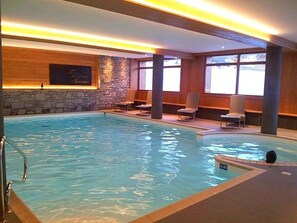 An indoor swimming pool with a stone wall, wooden paneling, and several lounge chairs.