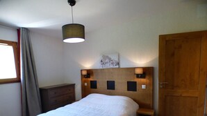 Une chambre à coucher avec un lit, une tête de lit en bois, des lampes de chevet, une table de chevet, une commode, une porte et une fenêtre avec des rideaux.