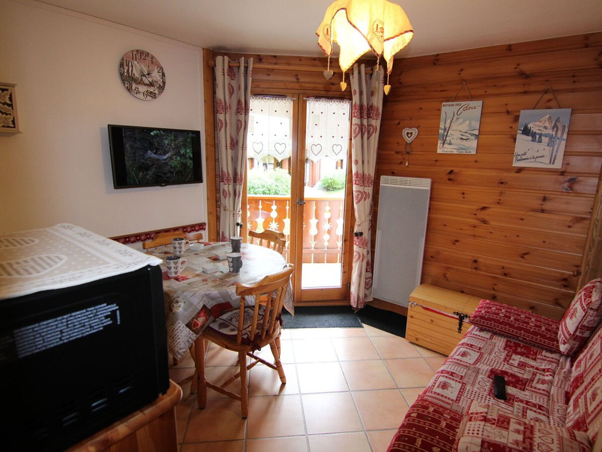 Una habitación acogedora con detalles de madera, una mesa de comedor con sillas, un sofá, un televisor y un radiador.