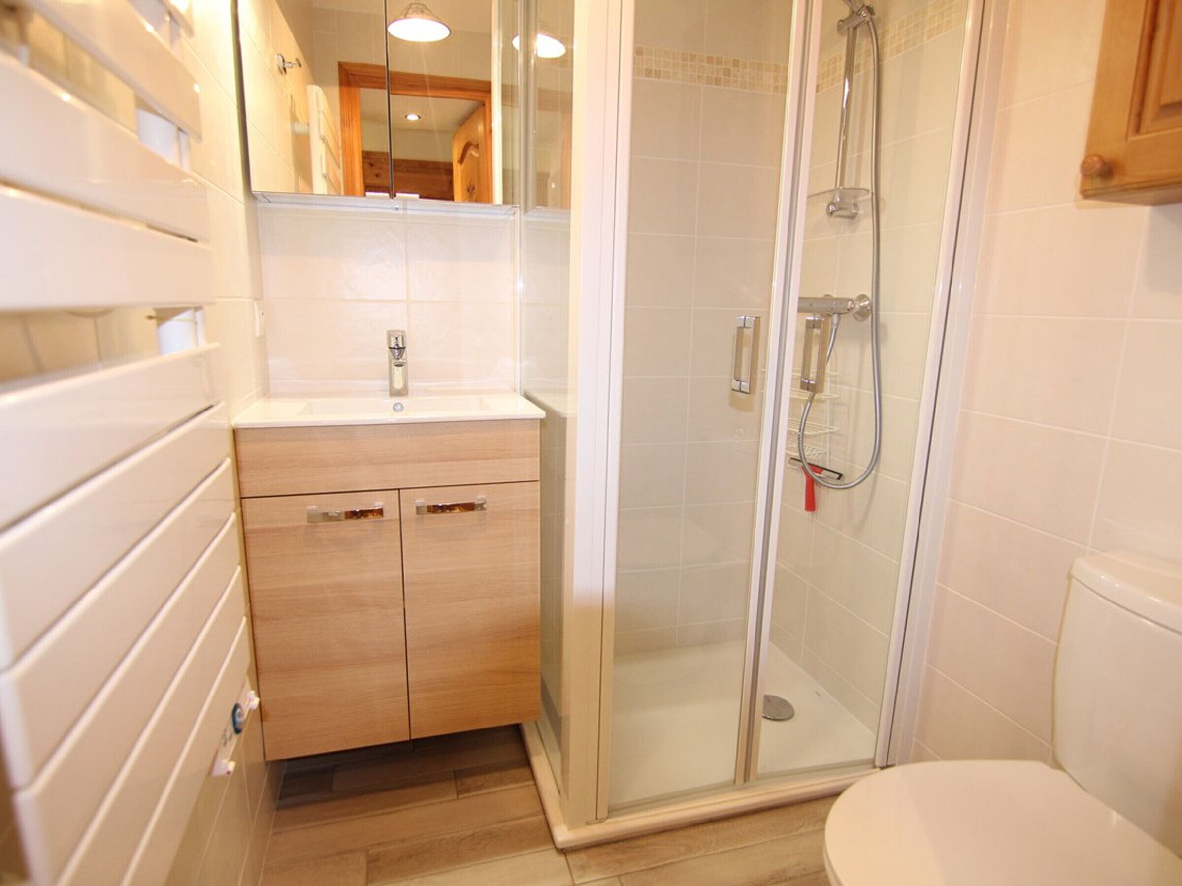 A modern bathroom with a glass-enclosed shower, a white sink, and wooden cabinetry.