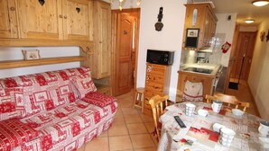 A cozy room with a patterned sofa, wooden cabinets, a kitchenette, and a dining area with a table set for two. - 2-room apartment for 4 people in Les Saisies (Les Saisies)