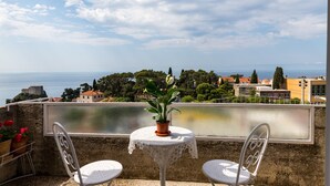 Un balcón con dos sillas blancas y una mesa, con vistas panorámicas al mar y a un pueblo.