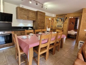 Een keuken met houten kastjes, een eettafel met geruit tafelkleed en een poster aan de muur.