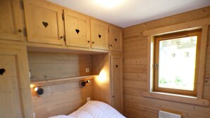 A wooden room with a bed, built-in cabinets with heart-shaped cutouts, a window with a view, and a wall-mounted light. - 5-room apartment for 8 ppl in Les Saisies (Les Saisies)