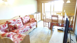 A cozy living room with a wooden sofa, a dining table with chairs, and a television. - 5-room apartment for 8 ppl in Les Saisies (Les Saisies)