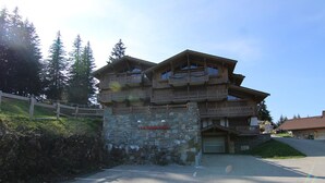 A multi-story wooden building with balconies, a stone wall entrance, and a parking area. - 5-room apartment for 8 ppl in Les Saisies (Les Saisies)