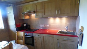 A kitchen with wooden cabinets, a red countertop, a sink, a stove, and an oven. - 5-room apartment for 8 ppl in Les Saisies (Les Saisies)