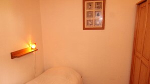 A small, neatly made room with a single bed, a wooden cabinet, and a wall-mounted shelf with a light. - Studio cabin Les Saisies 6 people, near center (Les Saisies)