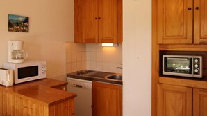 A compact kitchen with wooden cabinets, a coffee maker, a microwave, and a dishwasher. - Studio cabin Les Saisies 6 people, near center (Les Saisies)