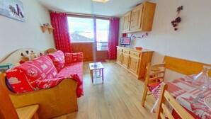 A cozy room with a wooden sofa, a small table, a wooden cabinet, and a bed with a red patterned cover. - Studio cabin 4 pers, balcony, in Les Saisies (Les Saisies)
