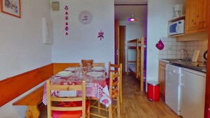 A dining area with a wooden table set for four, a kitchen with basic appliances, and a hallway leading to a bunk bed. - Studio cabin 4 pers, balcony, in Les Saisies (Les Saisies)
