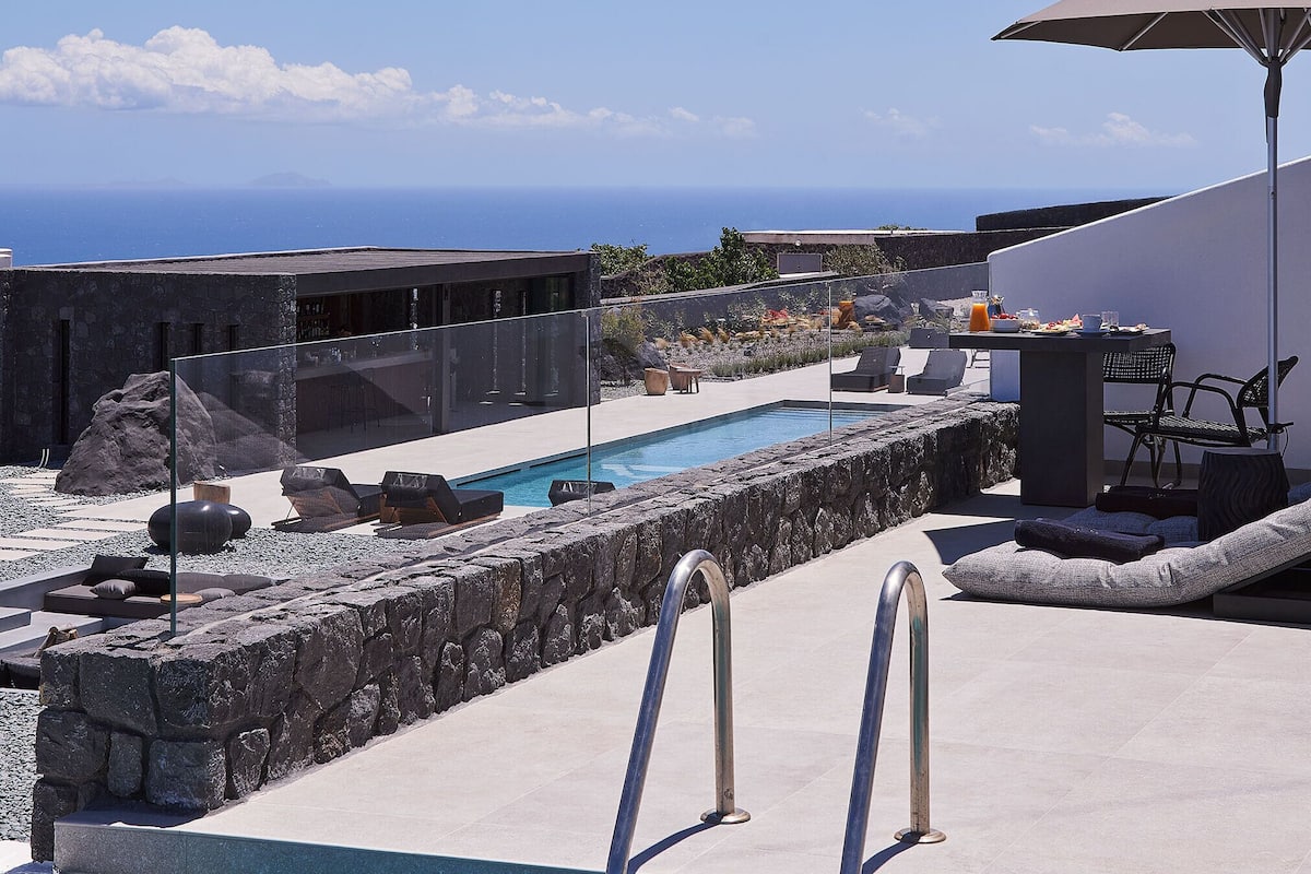 A pool area with a clear view of the ocean, stone walls, and lounge chairs.