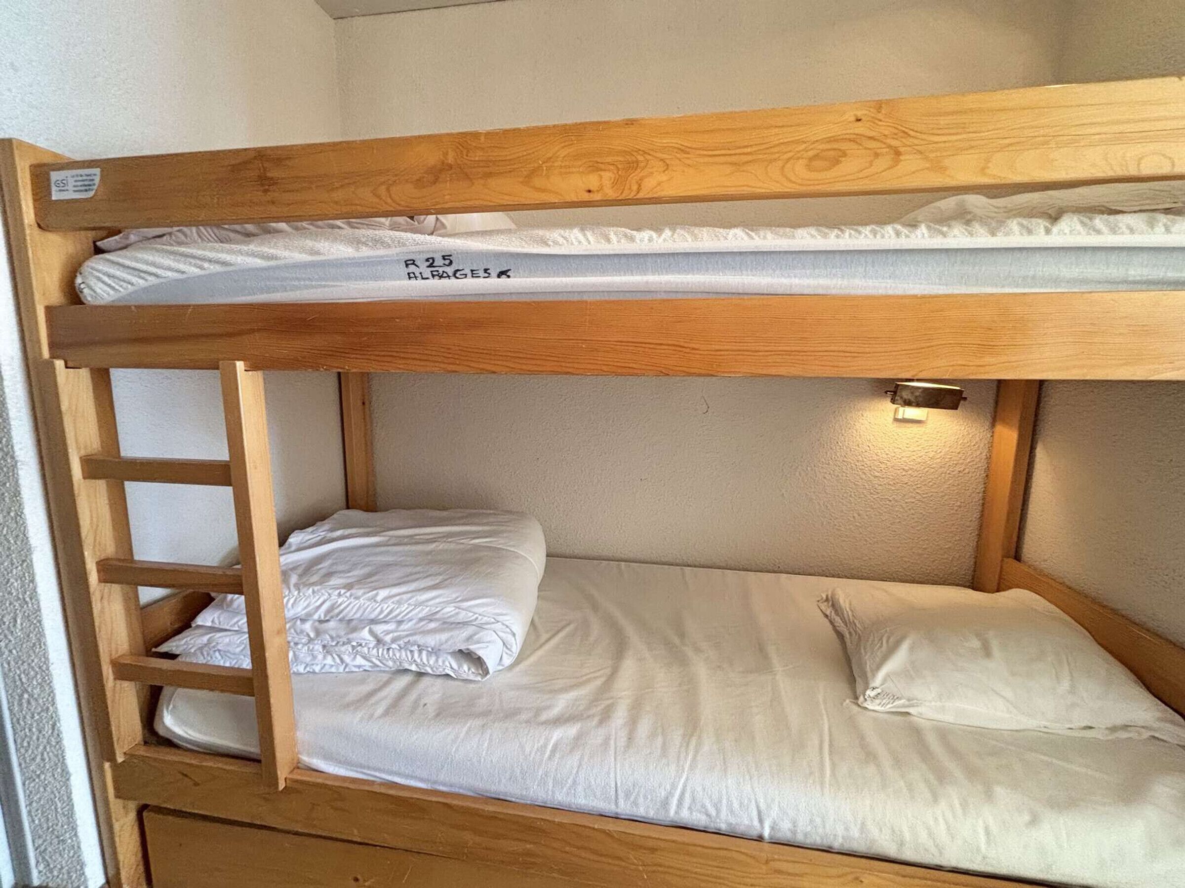 A bunk bed with a wooden frame, white bedding, and a small shelf on the left side.