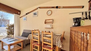 A cozy room with a wooden table and chairs, a sofa, a clock, and ski equipment on the wall. - Studio at the foot of the slopes in Notre-Dame-de-Bellecombe (Notre-Dame-de-Bellecombe)