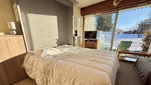 A bedroom with a large bed, a TV, and a view of a snowy landscape through a large window. - Studio at the foot of the slopes in Notre-Dame-de-Bellecombe (Notre-Dame-de-Bellecombe)