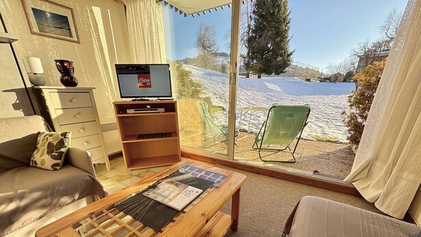 A cozy living room with a wooden coffee table, a sofa, a TV, and a view of a snowy landscape through large windows. - Studio at the foot of the slopes in Notre-Dame-de-Bellecombe (Notre-Dame-de-Bellecombe)