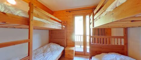A dormitory room with bunk beds, wooden walls, and a window.