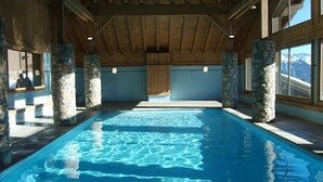 An indoor swimming pool with stone pillars, wooden beams, and large windows.