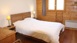 A wooden-paneled bedroom with a bed, two bedside lamps, a window with curtains, and a radiator.