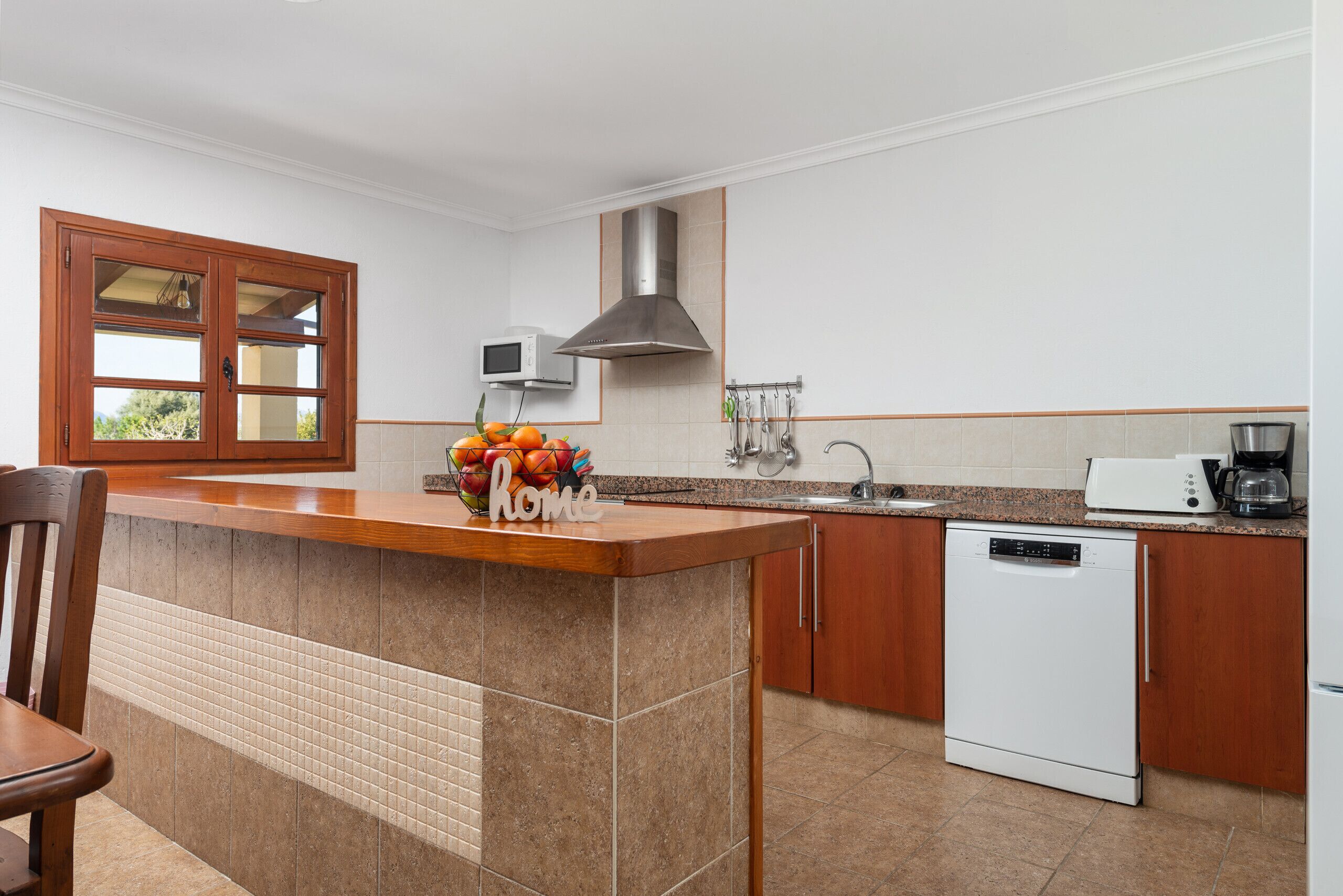 Una cocina con una isla de madera, lavavajillas, microondas y frutero.