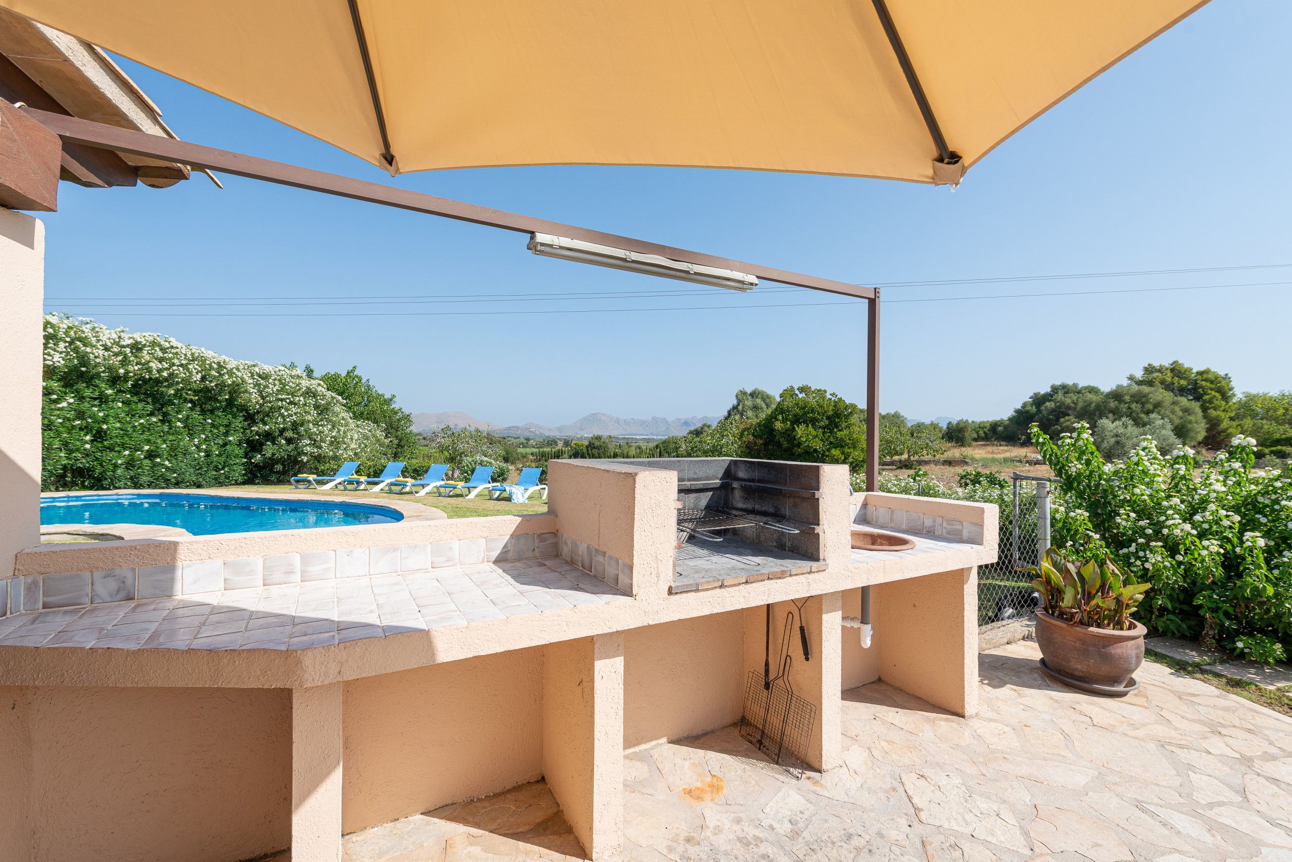 An outdoor barbecue area with a pool and lounge chairs in the background.