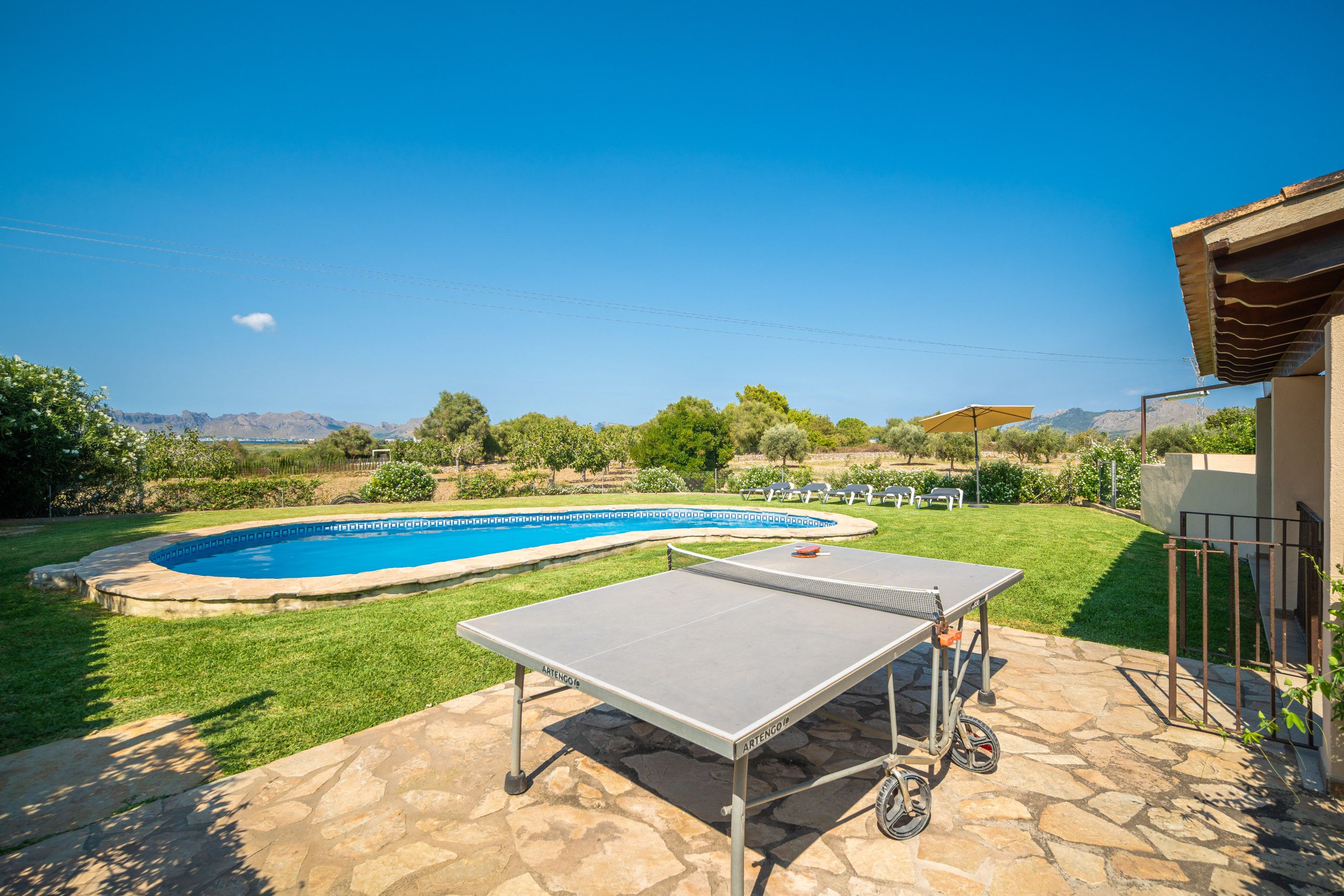 Una piscina con un área verde circundante, una mesa de ping pong y vistas a montañas en la distancia.
