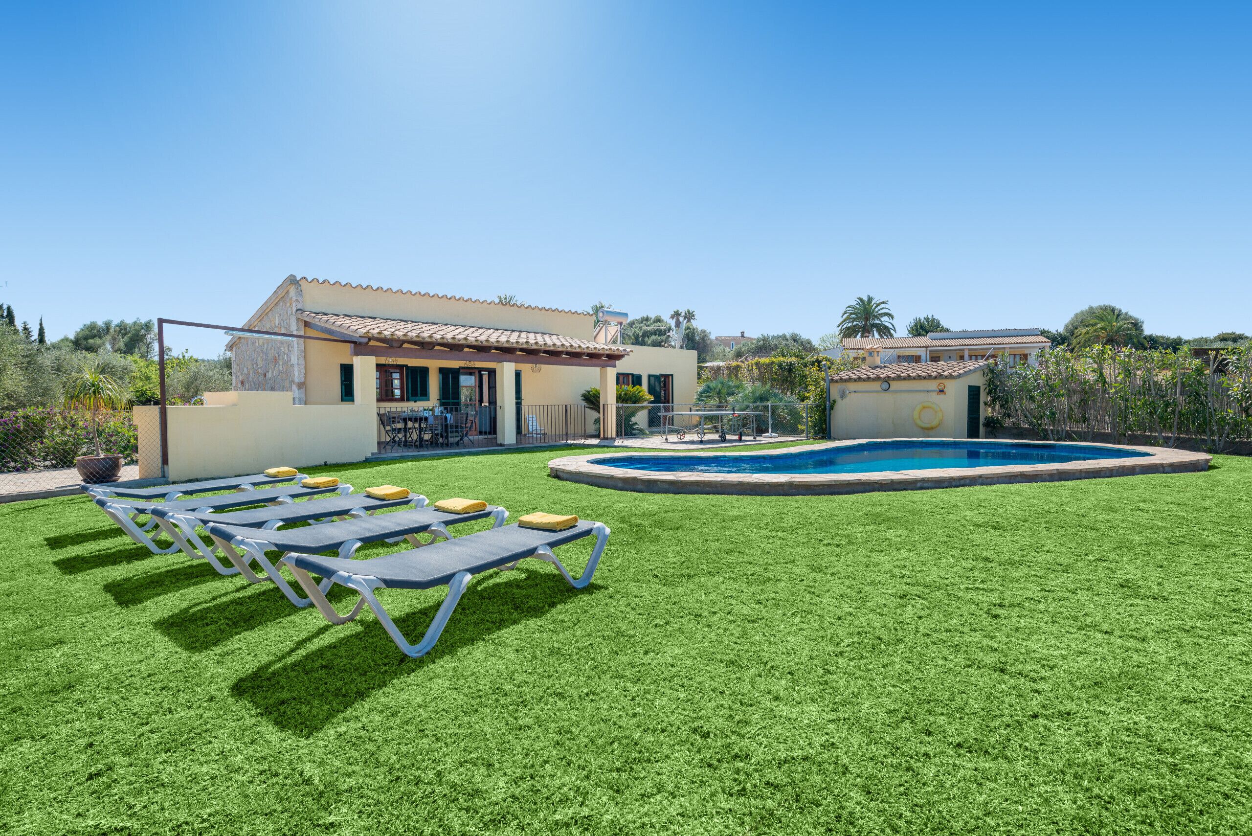 Une piscine entourée de chaises longues, avec une maison en arrière-plan.