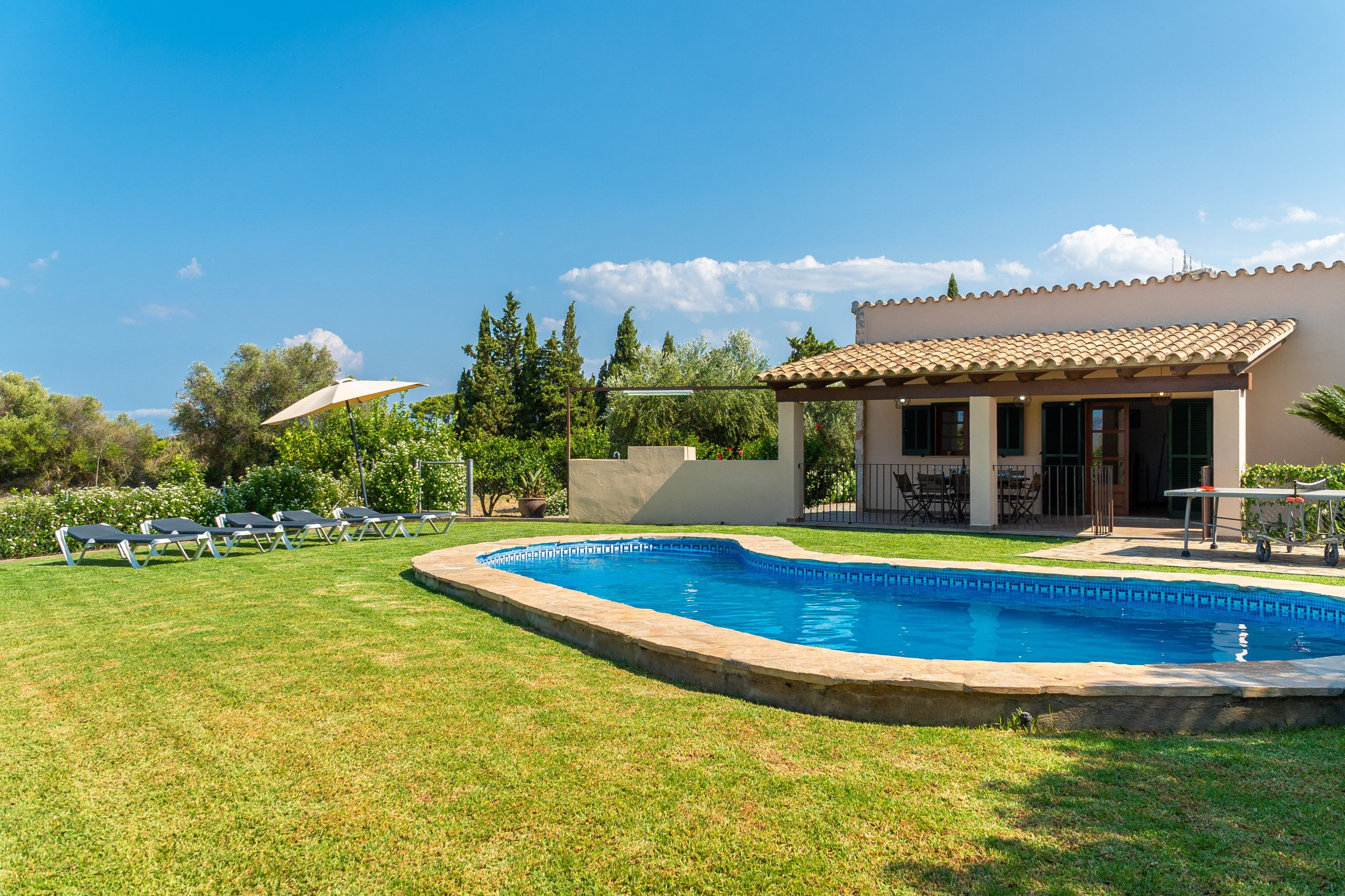 A swimming pool with a tiled deck, a covered patio area, and lounge chairs.