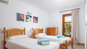 Een kamer met twee houten bedden, een houten dressoir en een raam met gordijnen.