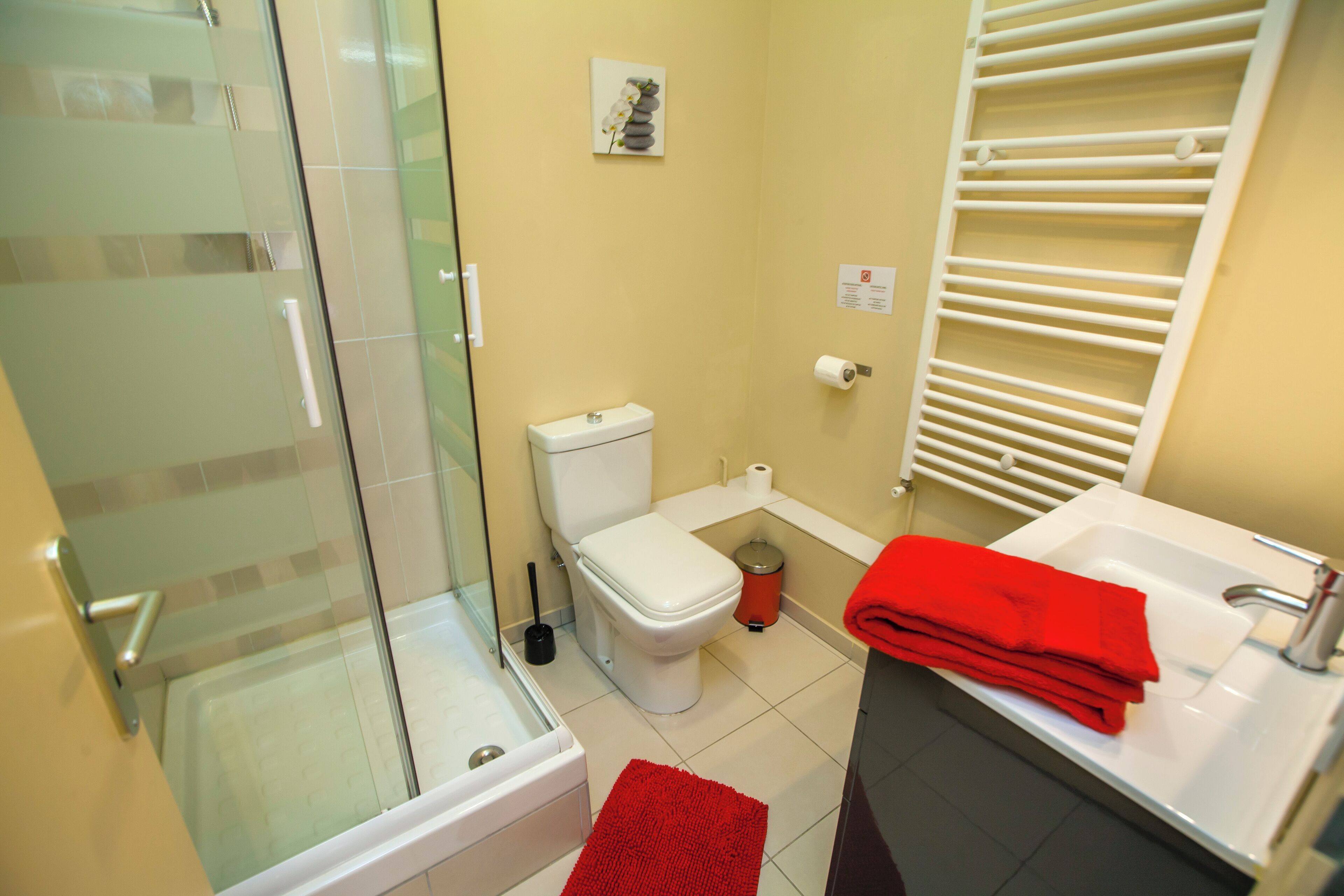 A bathroom with a glass shower enclosure, a toilet, a sink, and a red towel on the counter.