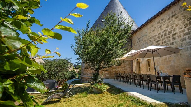 A courtyard with stone buildings, a large umbrella, and outdoor seating. - Large gîte with indoor pool and sauna (Charbogne)